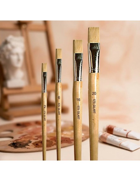 Pinceles planos Gilart serie 579 en mesa de trabajo con paleta y tubos de pintura al óleo